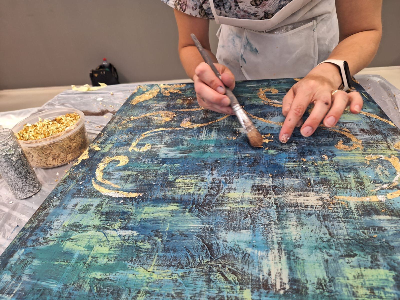 Mani al lavoro con il pennello sul decoro dorato della tela