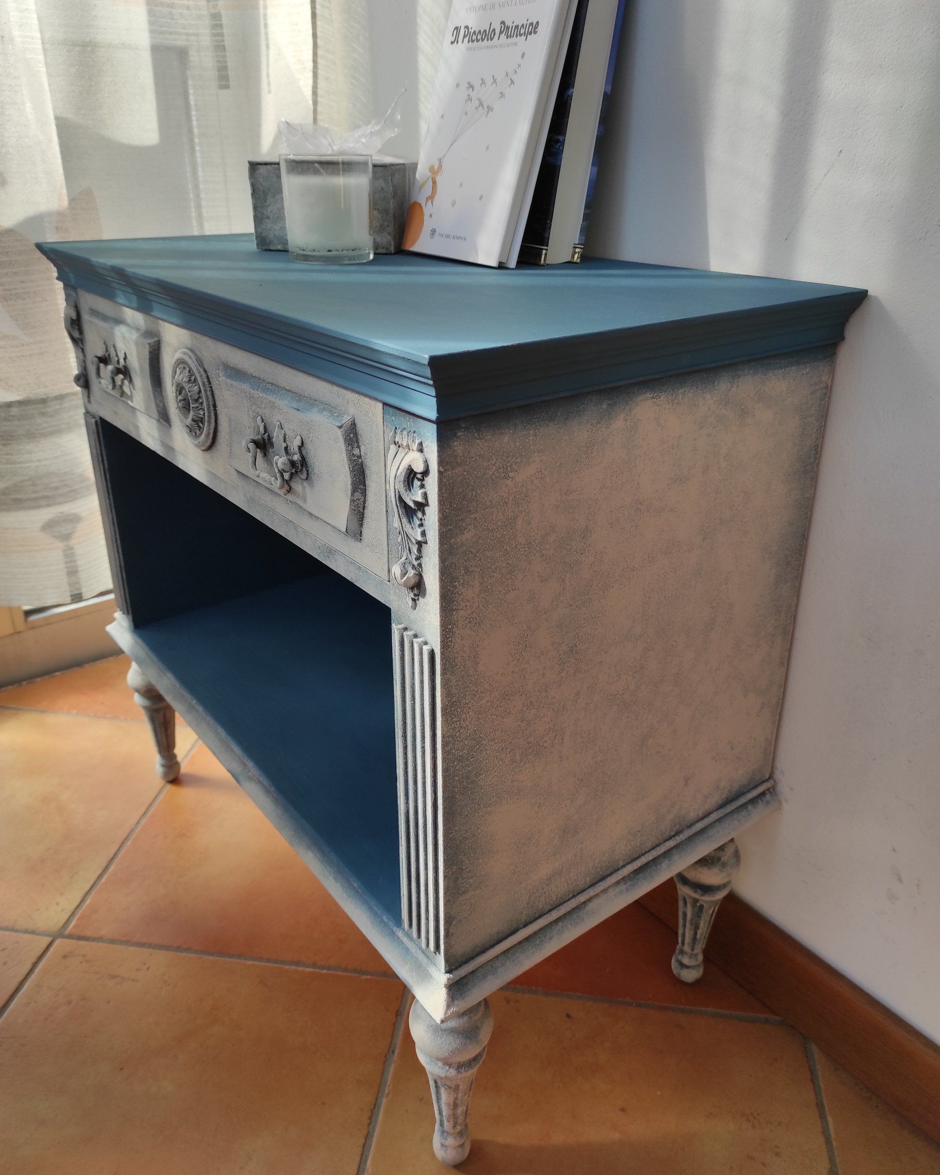 Comodino rinnovato visto di tre quarti: fianco materico chiaro e interno del vano blu