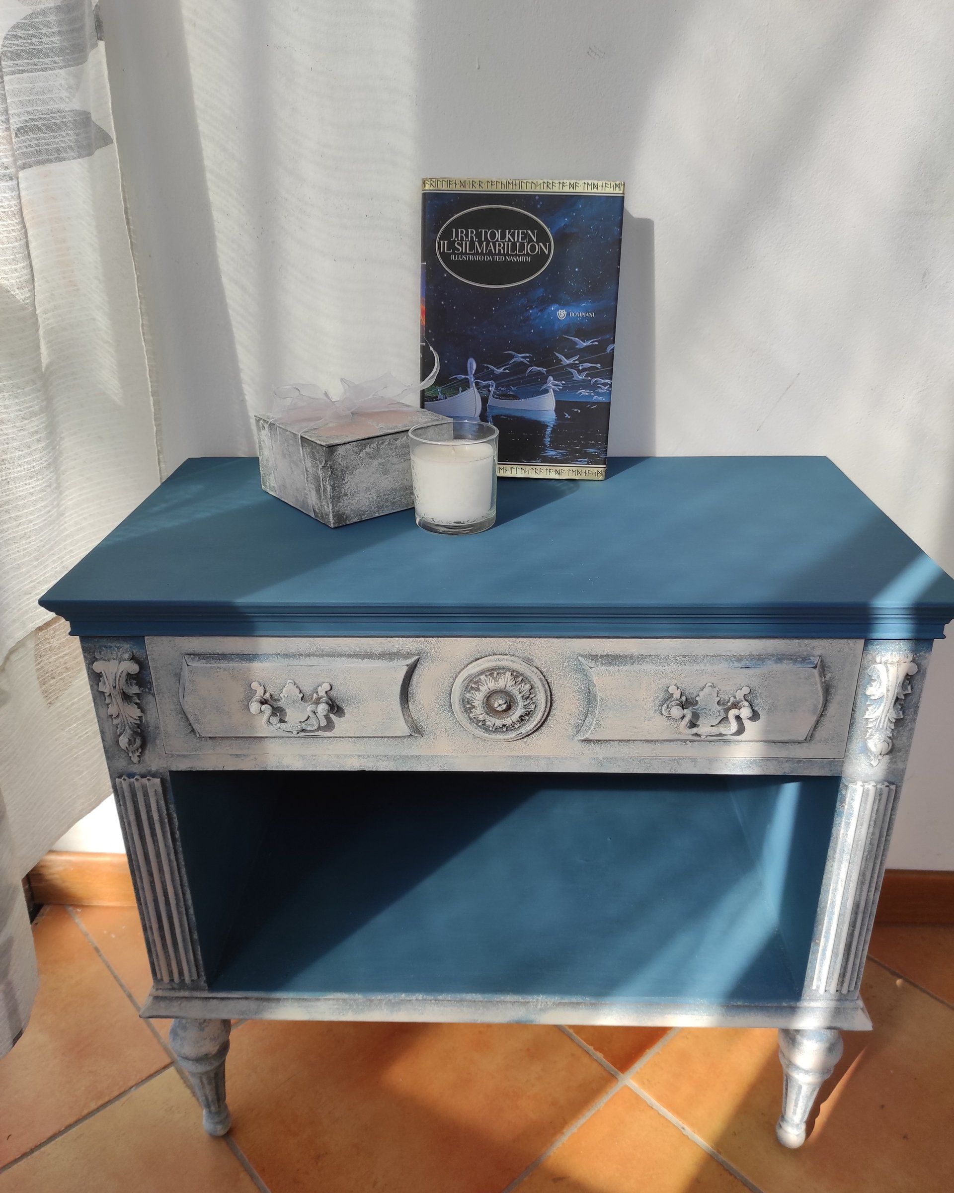 Comodino dopo il restyling: piano e vano a giorno blu, cassetto e struttura bianco-grigio materici con fregi in rilievo