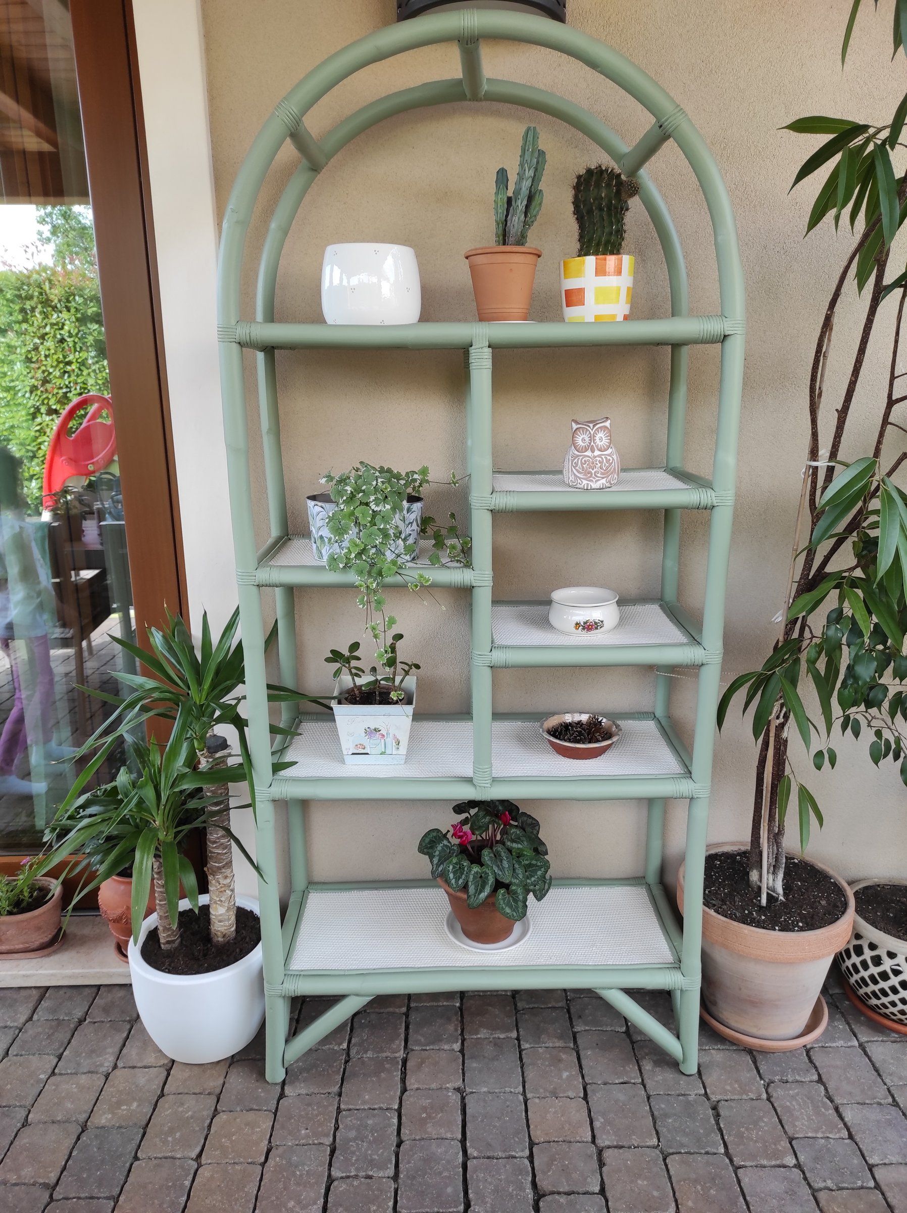 Scaffale in bamboo dopo il restyling: struttura verde salvia e ripiani avorio, sotto il portico con piante