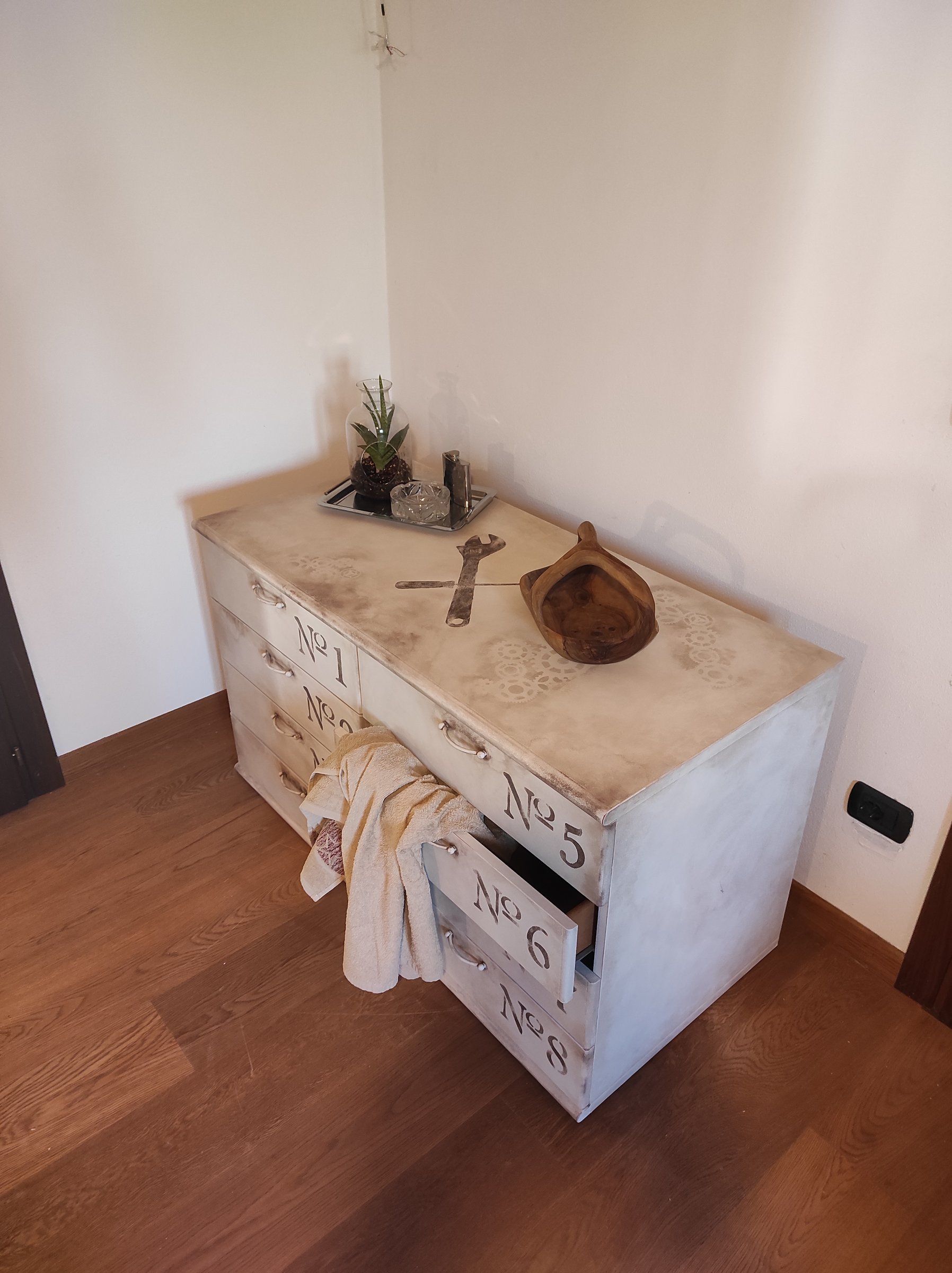 Cassettiera rinnovata nell'angolo di una stanza con parquet, con oggetti decorativi sul piano