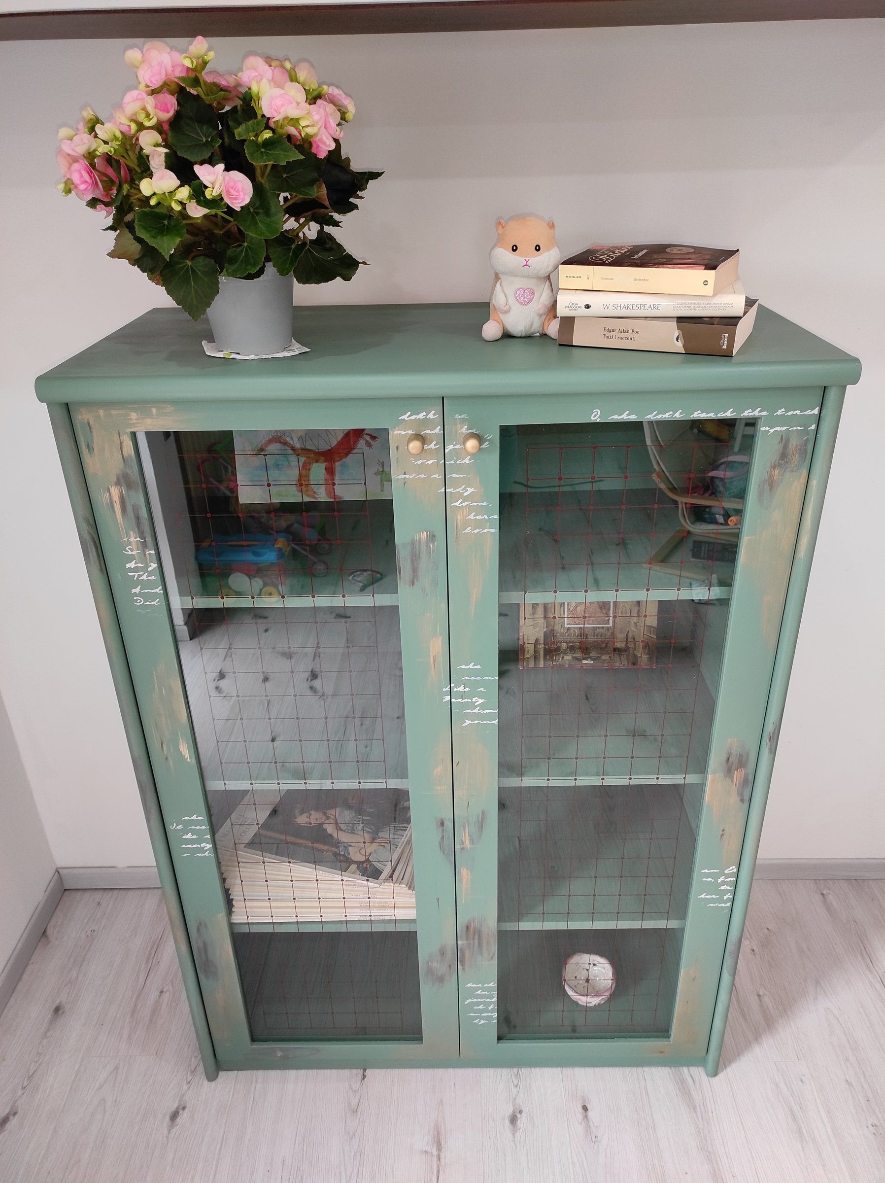 Vetrina con ante a vetri dopo il restyling: verde con velature scure e dorate, fiori sul piano