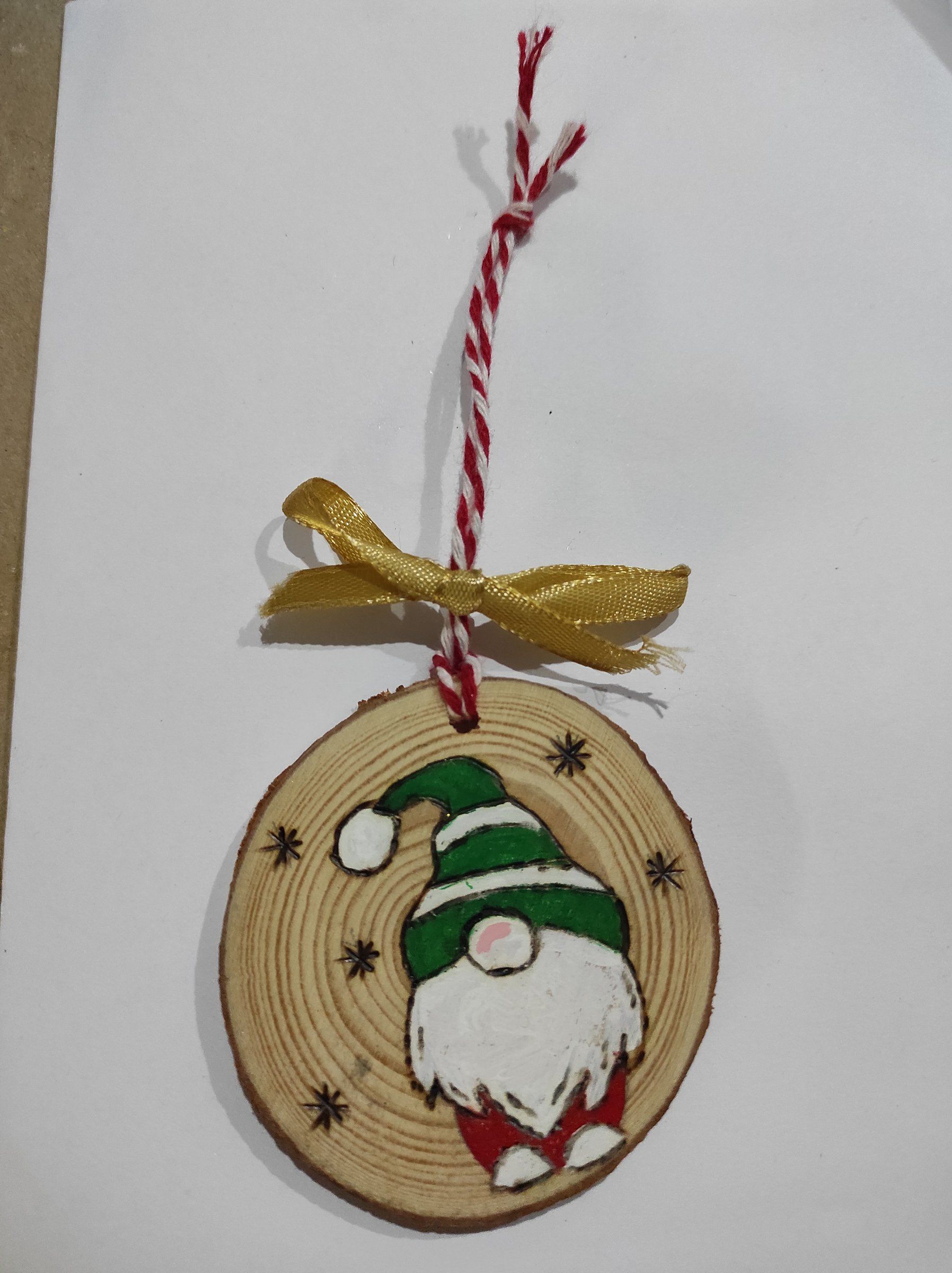 Fetta di legno dipinta con uno gnomo dal cappello verde, appesa a un nastro bianco e rosso