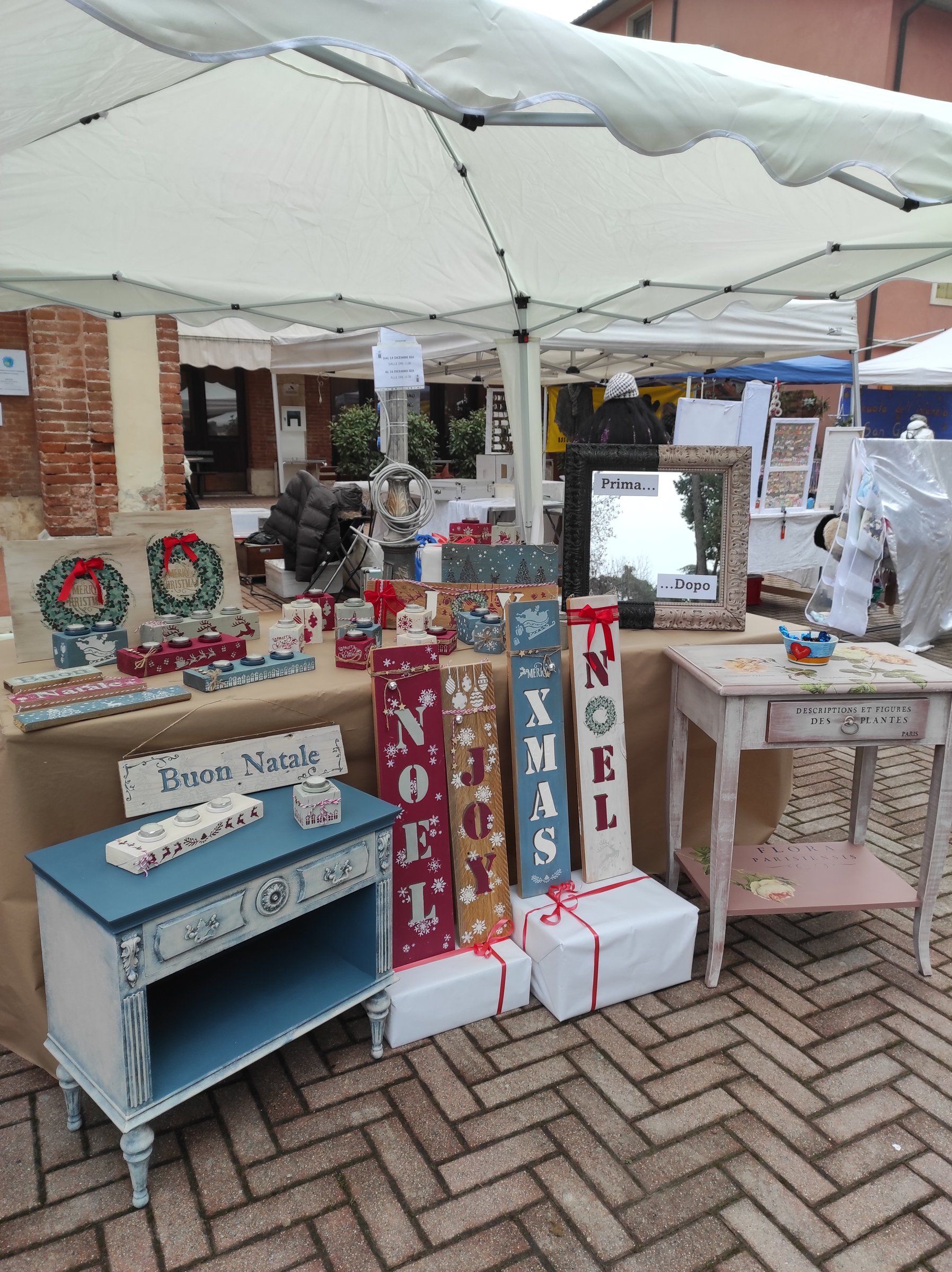 Lo stand sotto il gazebo con decorazioni natalizie dipinte, un comodino blu e un tavolino rosa decorato