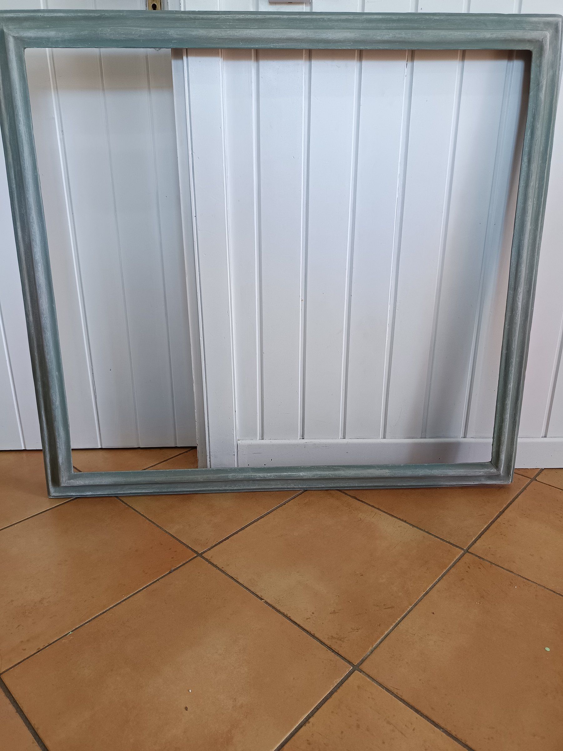 Grande cornice dopo il restyling, verde-grigio anticato, appoggiata a una porta bianca