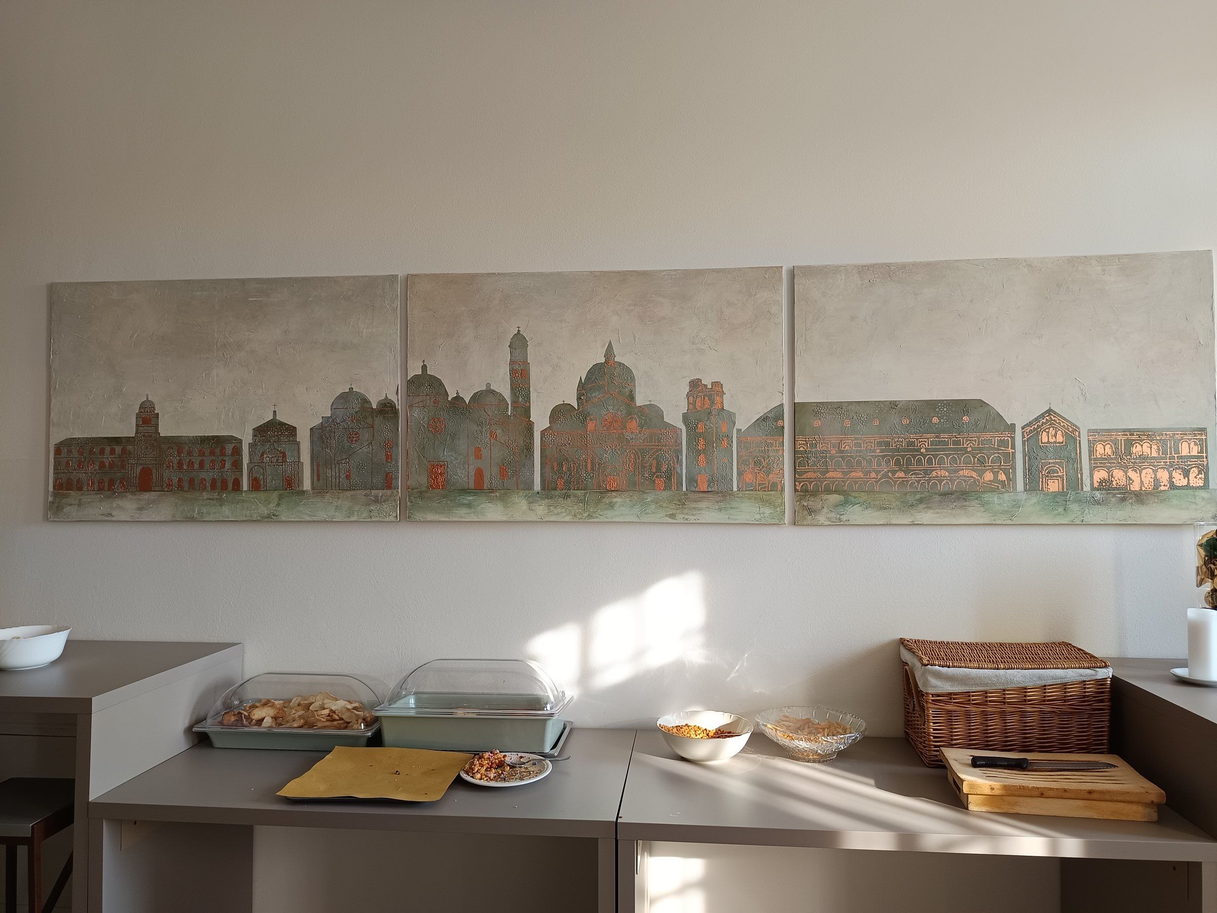 Tre grandi tele affiancate con lo skyline di Padova: palazzi e basiliche in verde-grigio con dettagli ramati su fondo materico chiaro