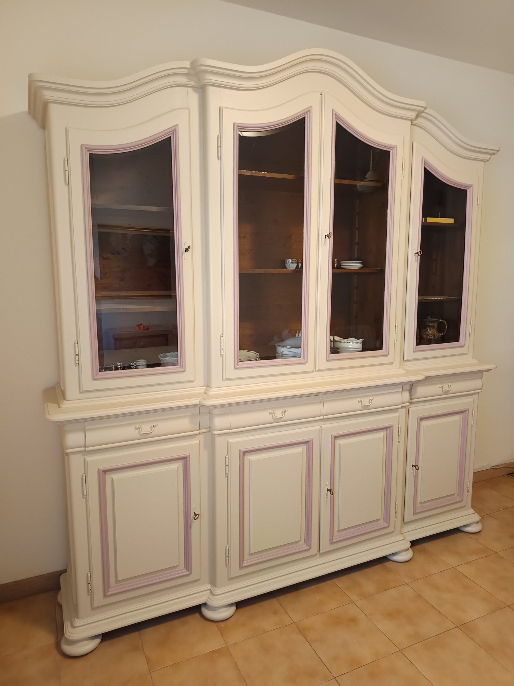 Credenza avorio con profili lilla vista di scorcio, cimasa ondulata e piedi a cipolla